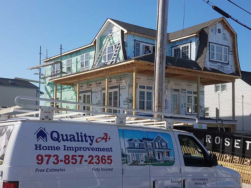 A Quality A+ Home Improvements work van parked in front of a large, two-story home they are installing new siding on