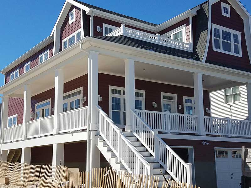 Large, two-story home with a deck area all around its exterior and red siding installed by Quality A+ Home Improvements